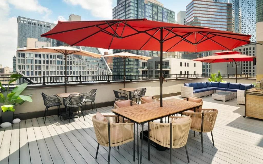 a patio with tables and chairs and a red umbrella at EVEN Hotel Long Island City - New York by IHG in Long Island City