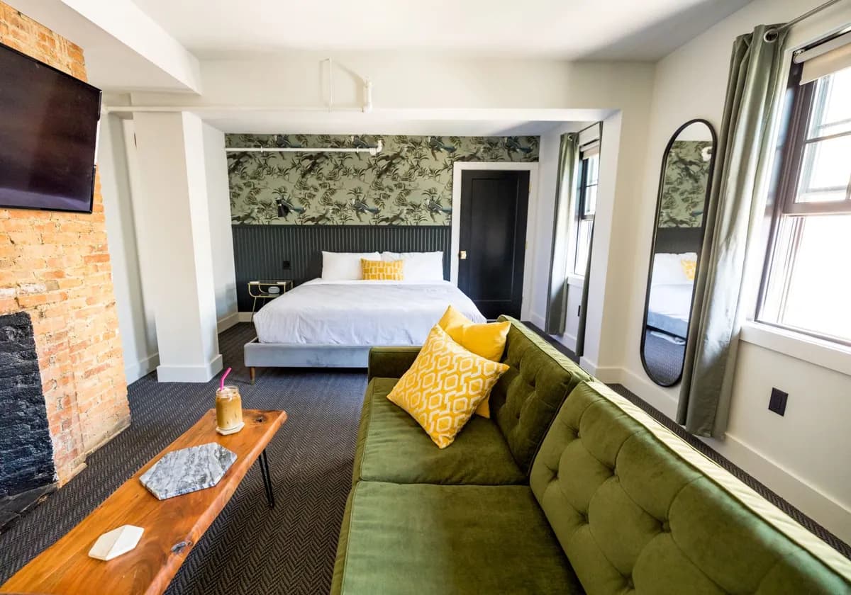 Stylish bedroom interior with a green sofa, patterned pillows, and a classic brick fireplace.