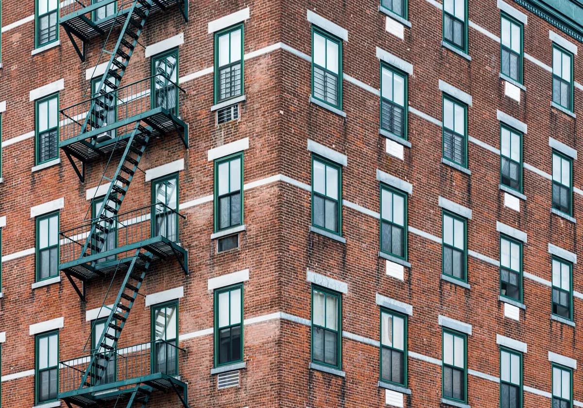 Corner view of a classic New York brick building featuring iconic fire escapes and windows.