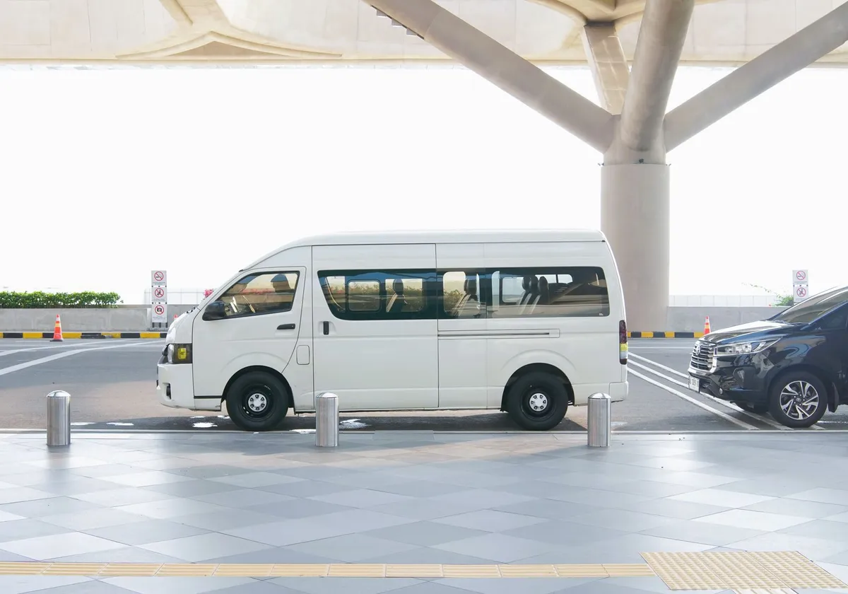 A white minivan parked at a modern airport terminal drop-off zone, ideal for travel and transport concepts.