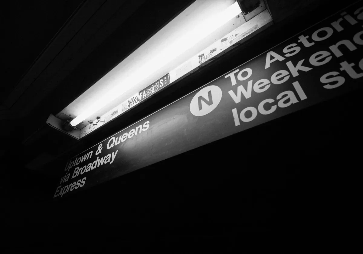 Black and white image of New York City subway signage for Queens and Broadway.