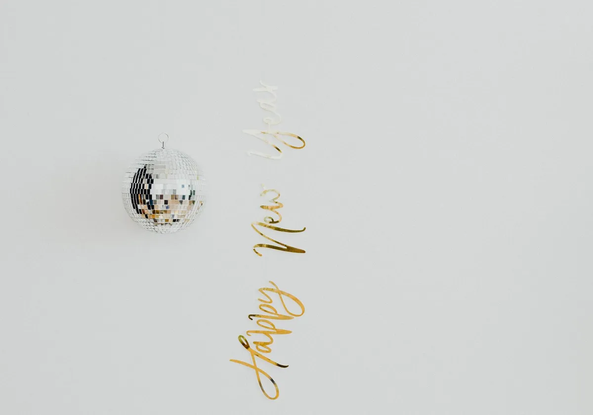Minimalist New Year decoration with a disco ball and gold text on a light background.