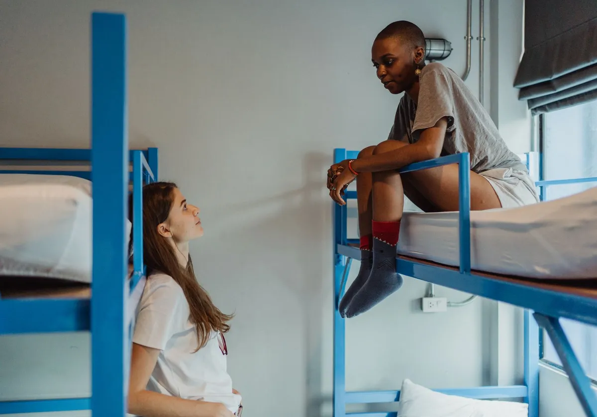 Two women having a friendly chat in a hostel bunk bed room, creating a relaxing atmosphere.