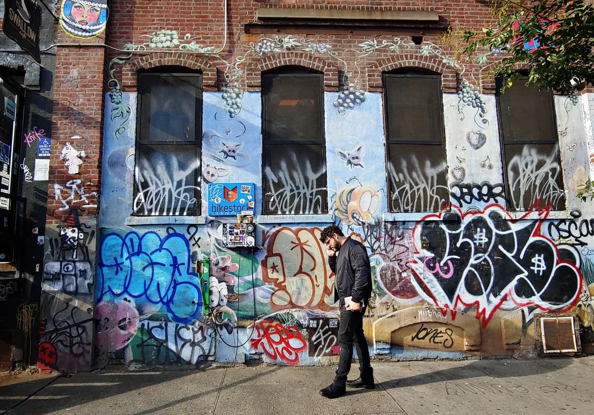Vibrant graffiti alley in Brooklyn with a person walking by, capturing urban street art culture.