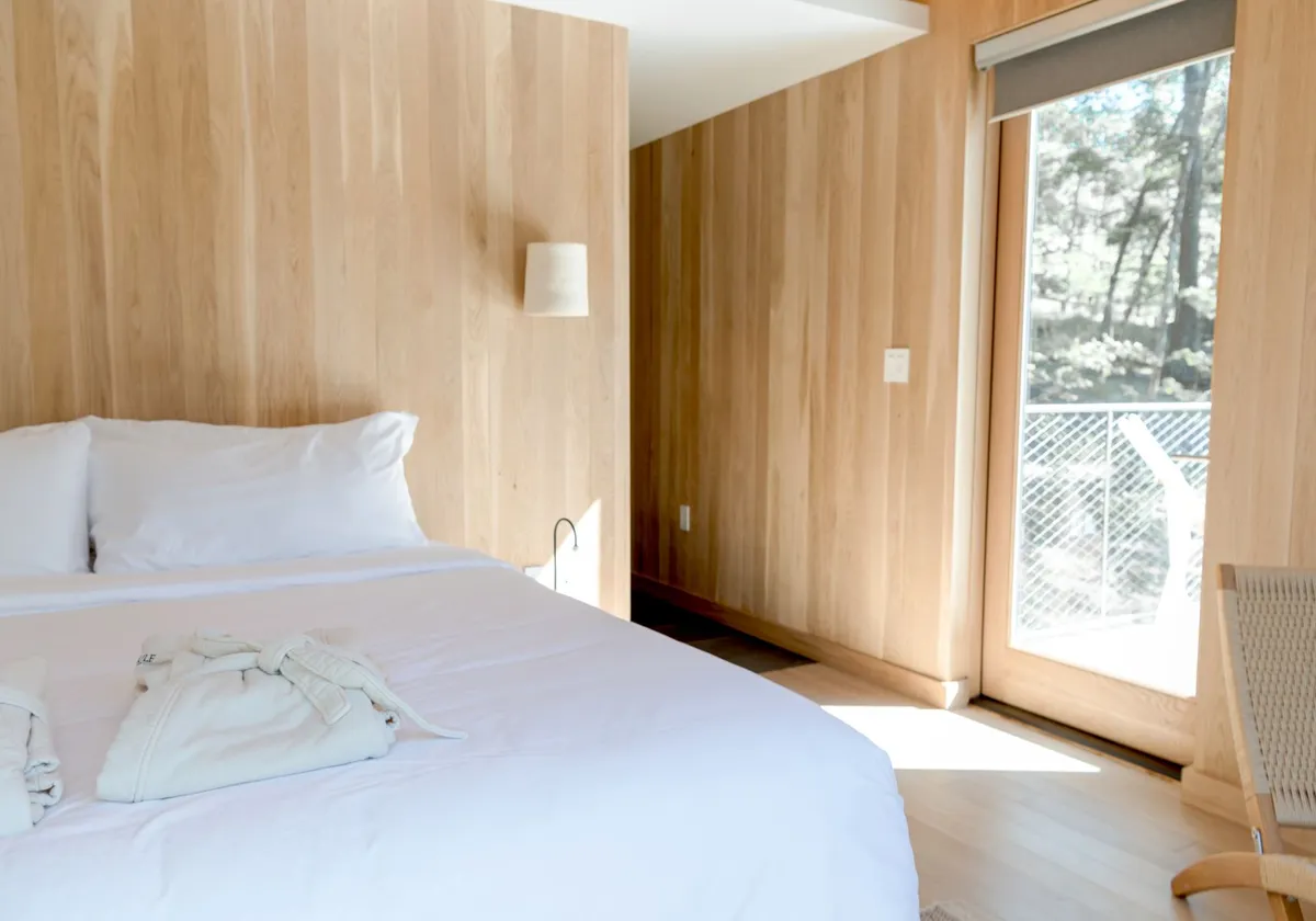 Bright minimalist bedroom with large windows, wooden walls, and a cozy bed, offering a peaceful retreat.