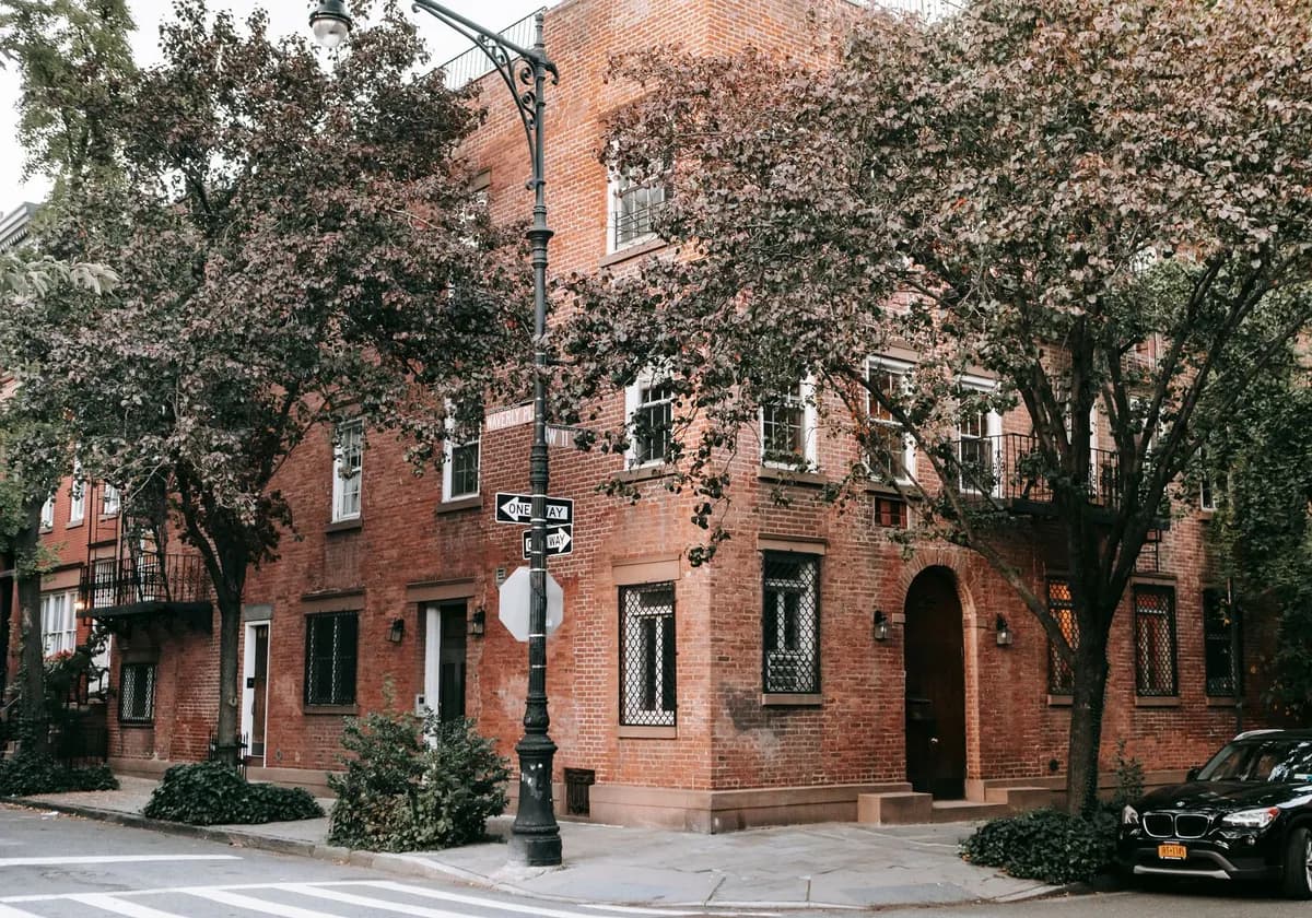 A quaint brick house surrounded by trees on a peaceful city street corner.