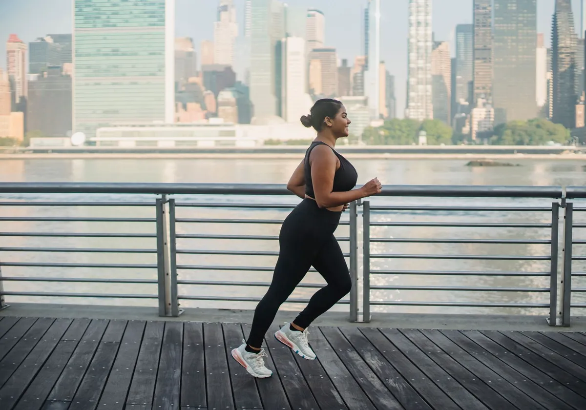 Woman running on boardwalk with city skyline background, promoting active and healthy lifestyle.