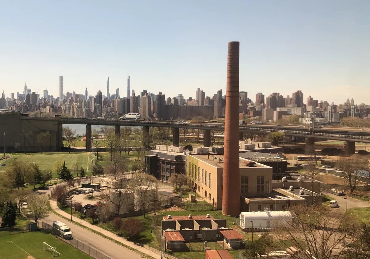 A panoramic view of New York City skyline with industrial structures and green spaces in the foreground.