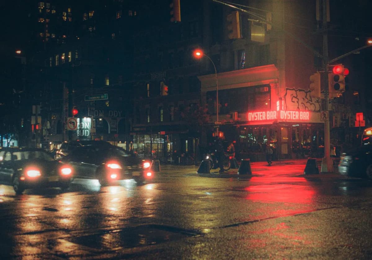 Glistening wet streets of NYC at night, featuring a vibrant oyster bar with red neon lights.