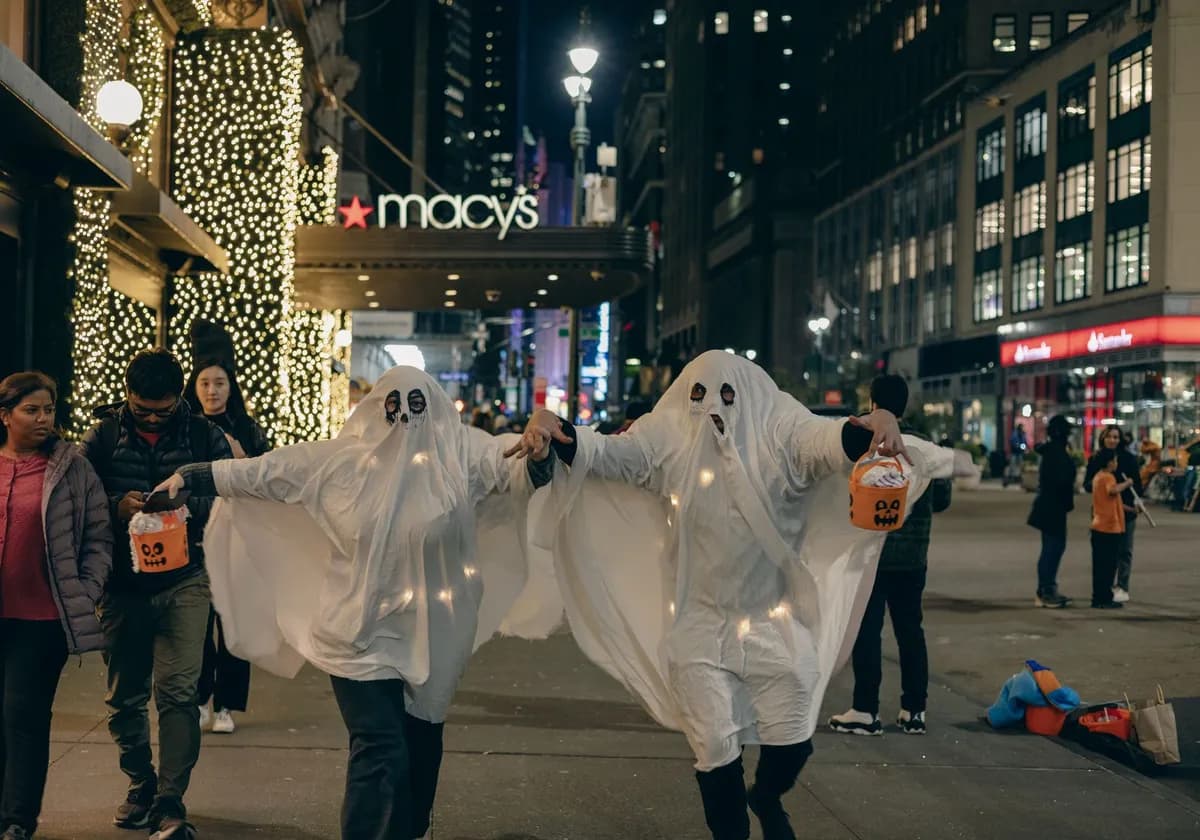 Adults in ghost costumes walk in New York City at night, celebrating Halloween.