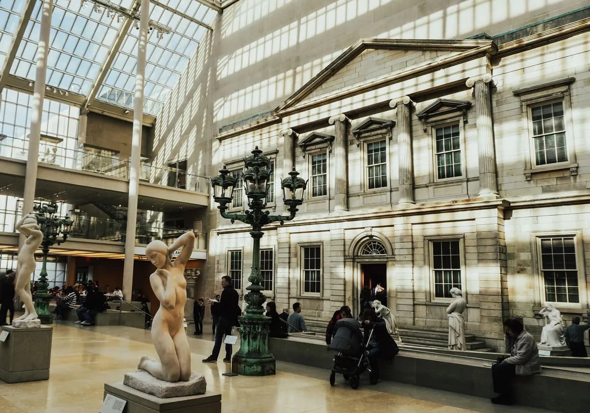 Sunlit atrium with statues and visitors at the Metropolitan Museum of Art, New York.
