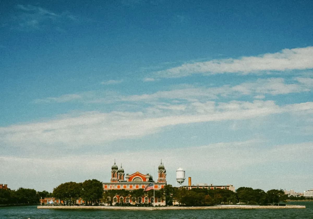 Scenic view of Ellis Island as the American flag waves, set against a clear blue sky.