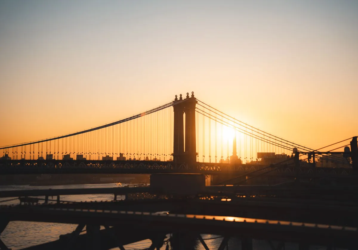 The sun rises majestically behind the iconic Manhattan Bridge, casting a warm glow over the New York City skyline.