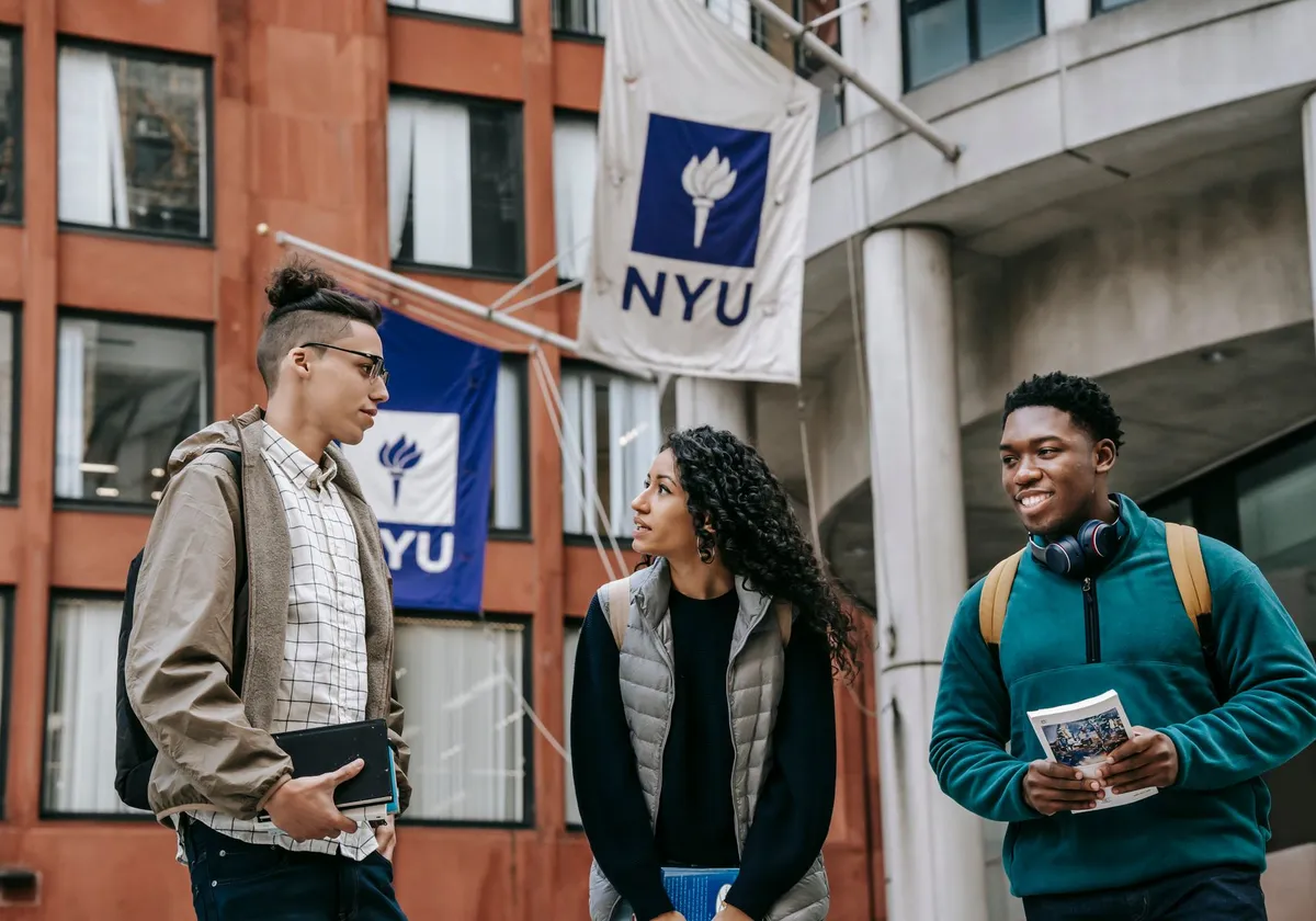 Group of diverse friends in casual clothes with papers standing near building and discussing details of university project