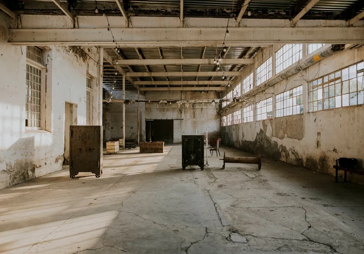 A spacious, dilapidated warehouse with exposed beams and aging furniture.