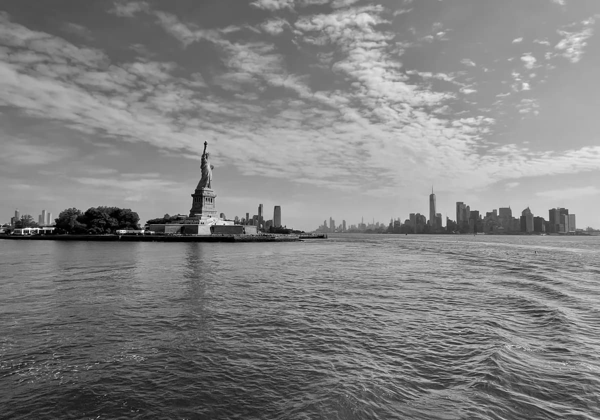 Black and white view of the Statue of Liberty with New York City skyline in the background.