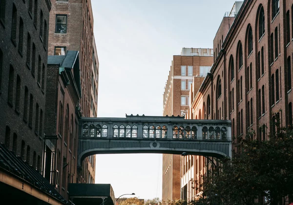 Narrow street with metal overpass connecting brick apartment houses against cloudless sky in city street in residential area on sunny day