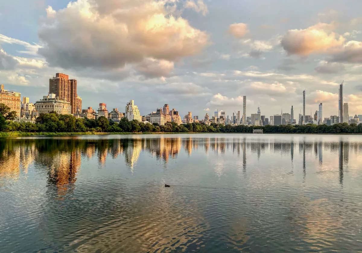 Central Park lake reflecting New York City skyline at sunset, capturing urban tranquility.