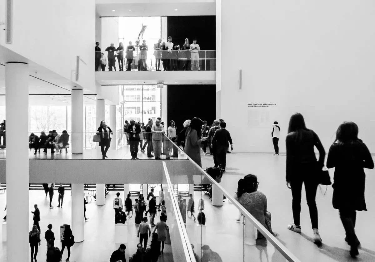 A dynamic black and white image of people in a modern museum setting.