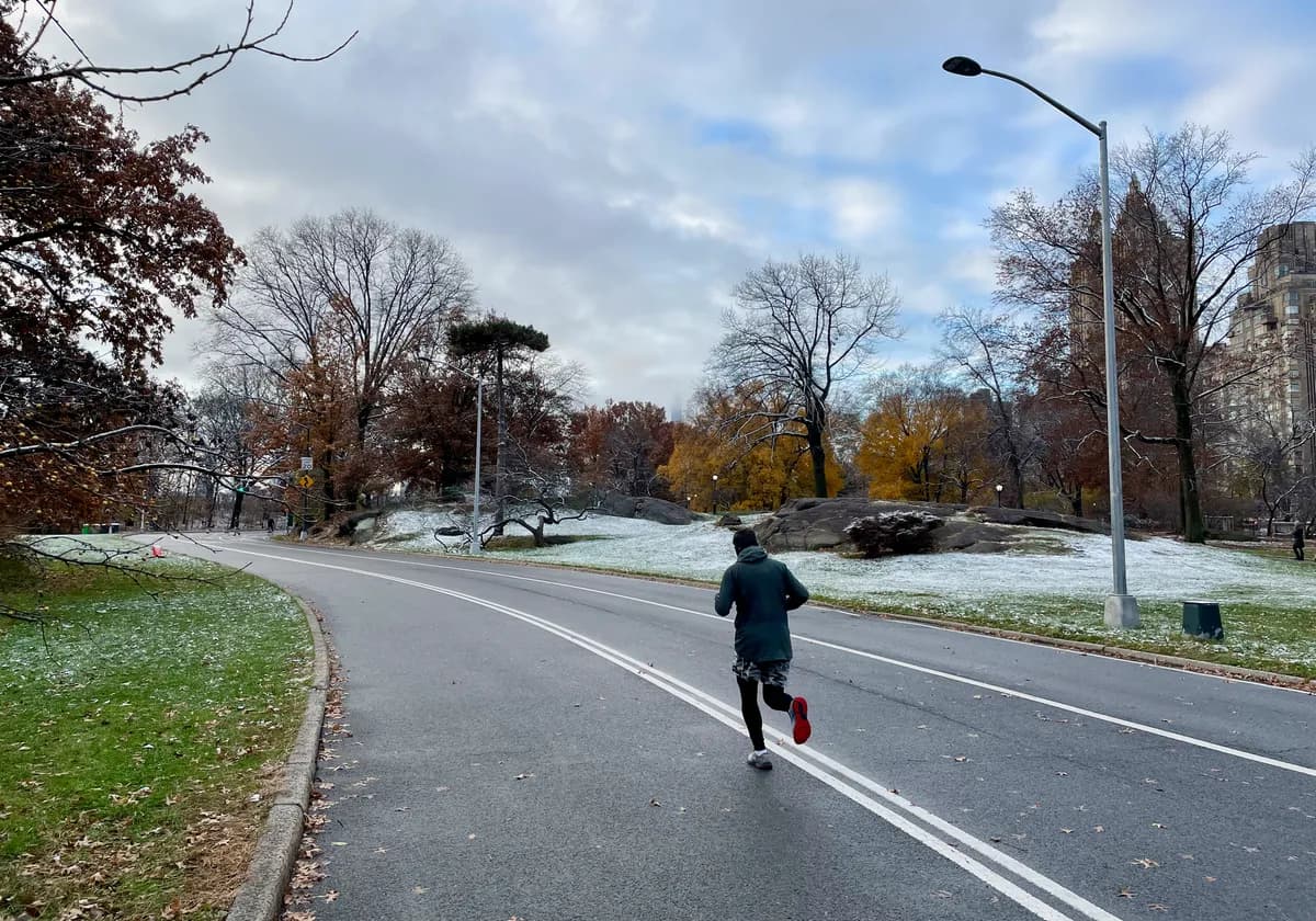 A lone jogger runs down a snowy road in Central Park, New York City.
