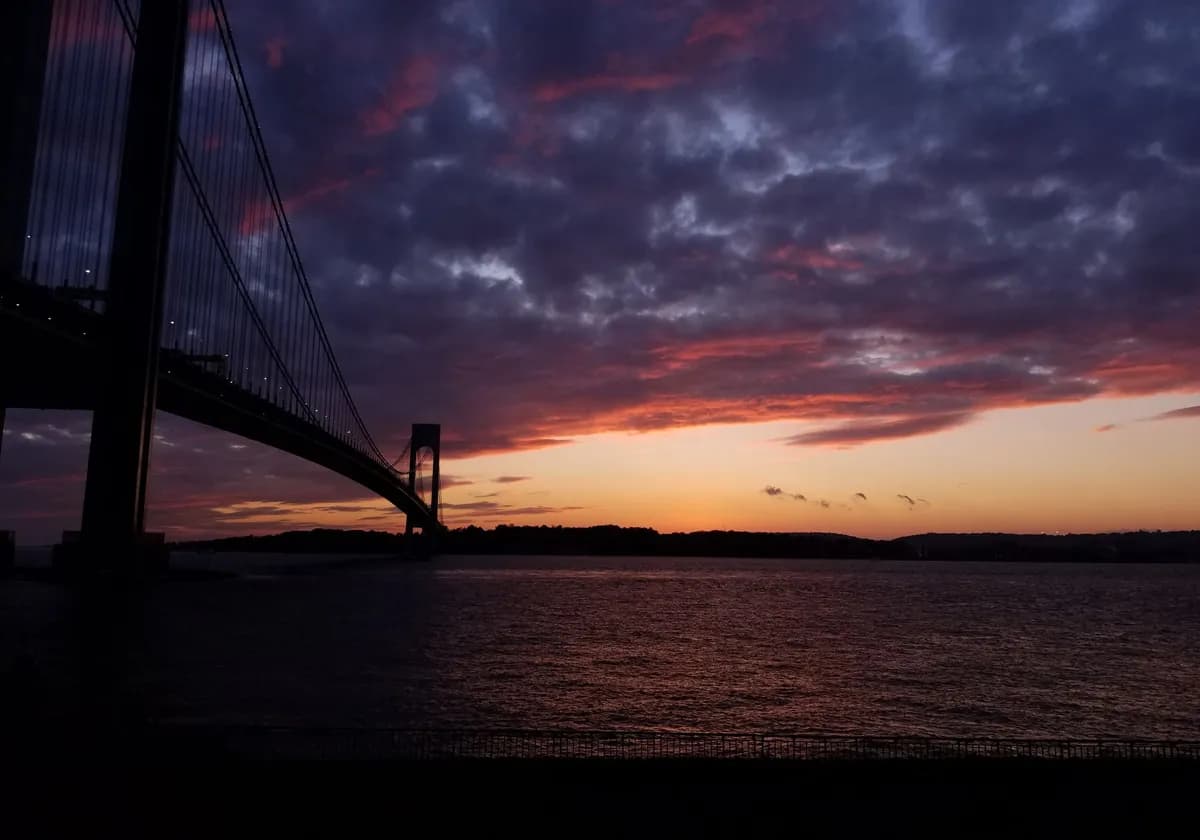 Stunning sunset view of the Verrazzano-Narrows Bridge with dramatic sky and silhouette effect.