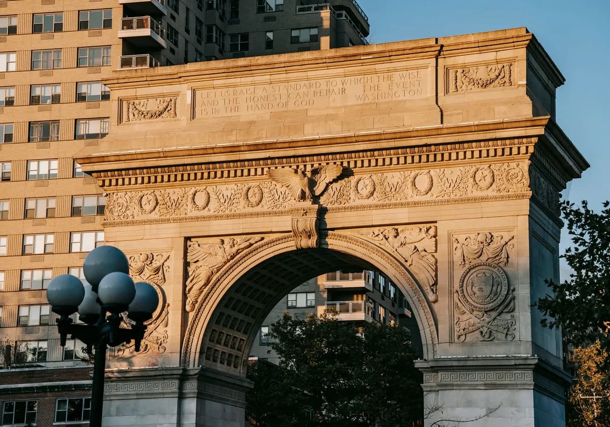 From below of aged triumphal arch placed in Washington Square Park in New York City against residential building illuminated by sunlight