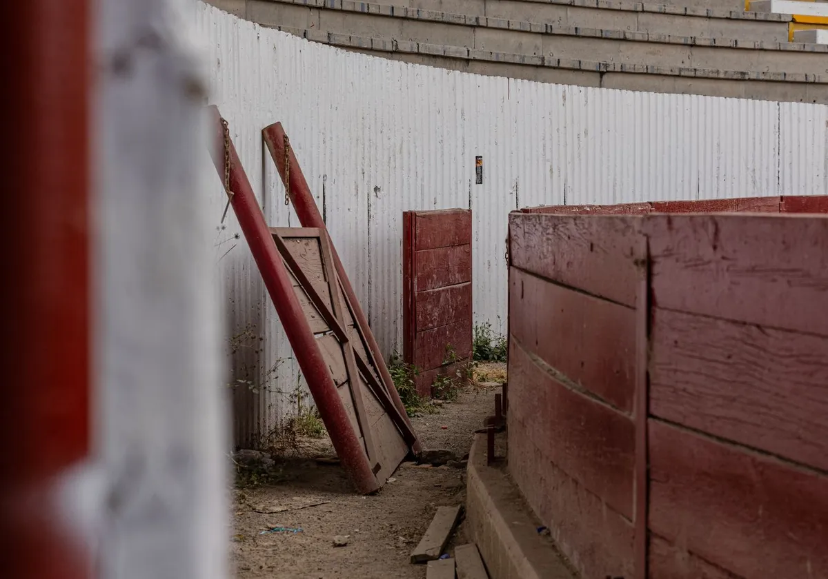 A rustic bullring area with red wooden gates and fences, showing wear.