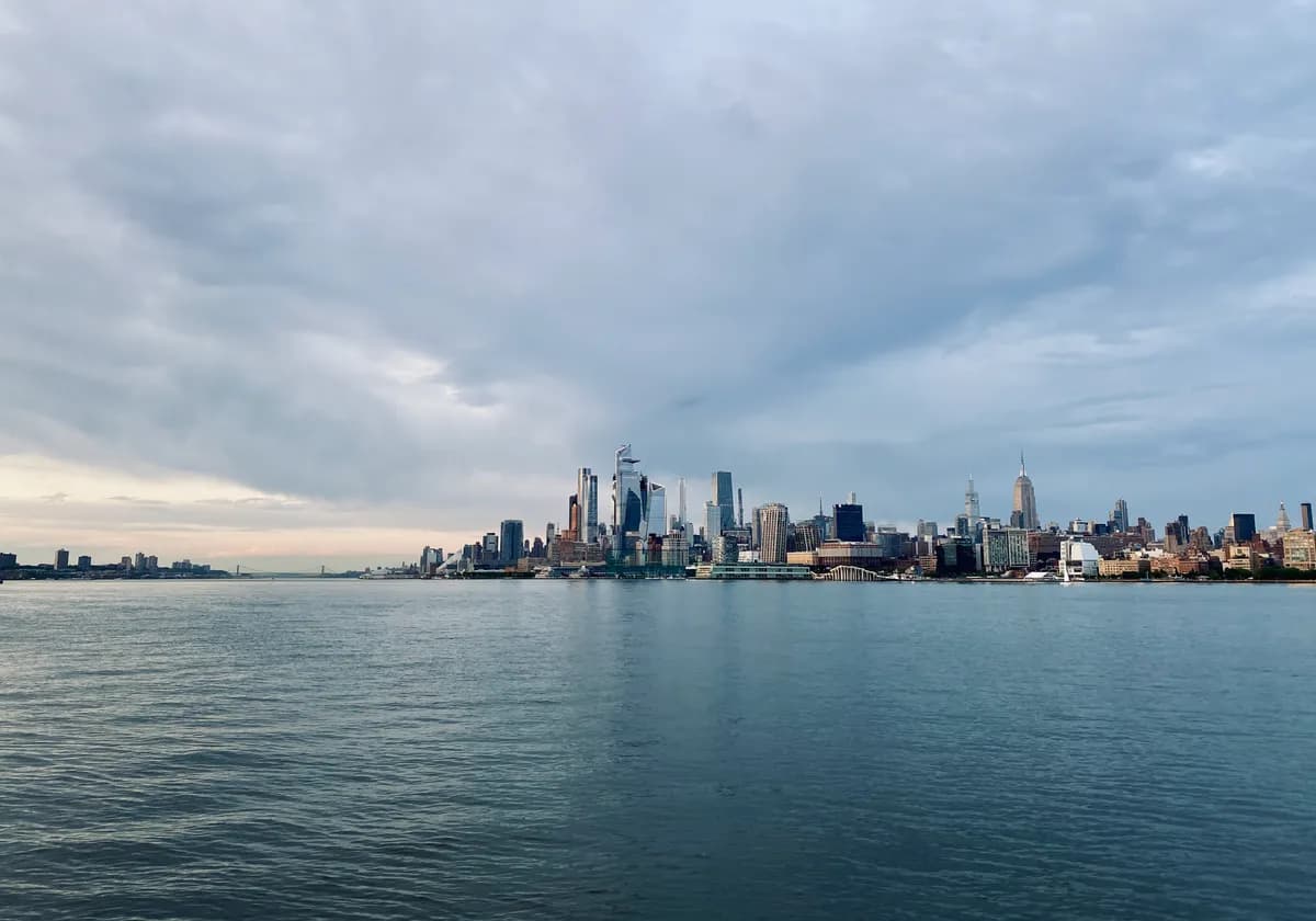Stunning view of New York City skyline across the river under a cloudy sky.
