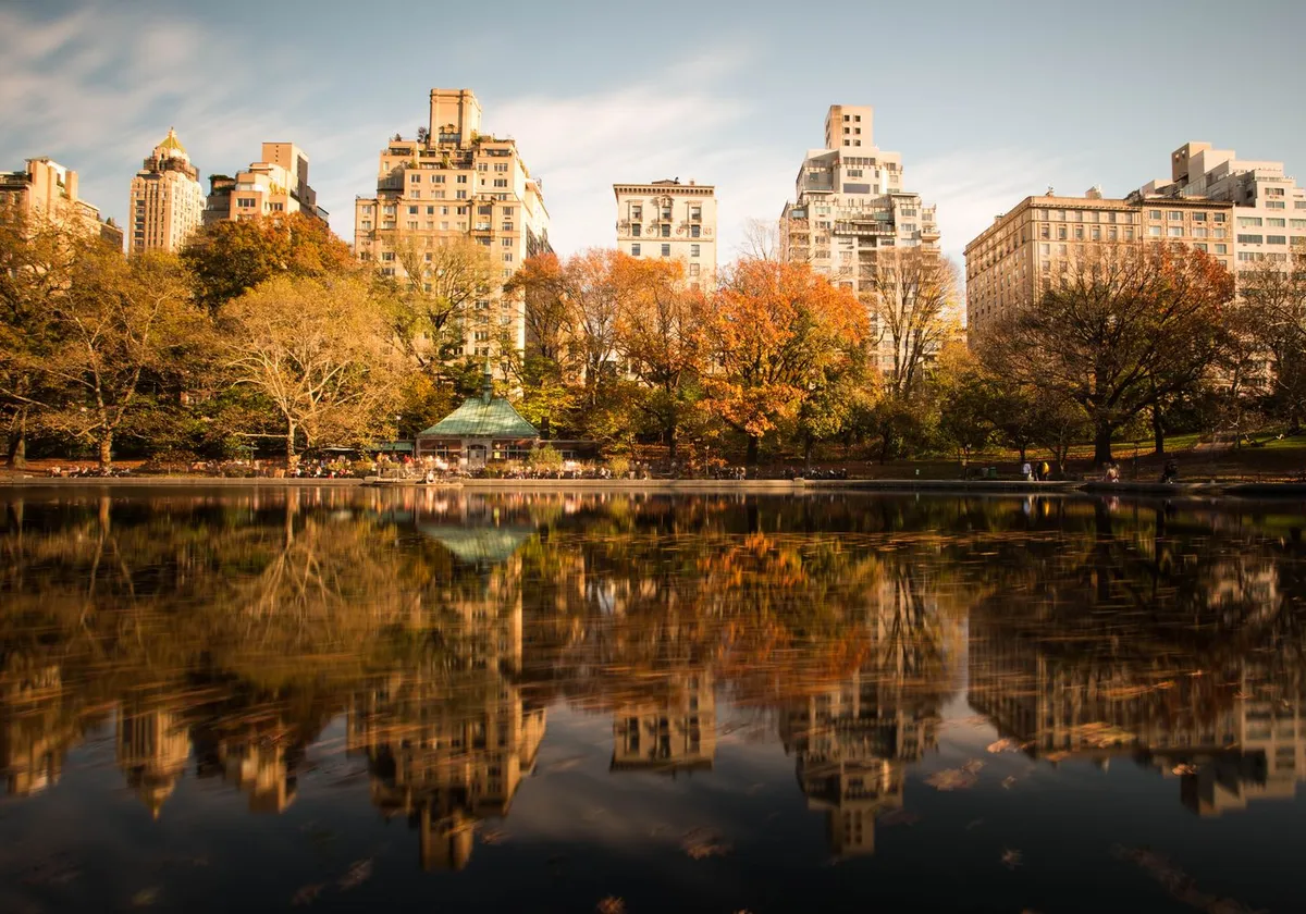 Stunning autumn view of Central Park with cityscape reflecting in the lake.