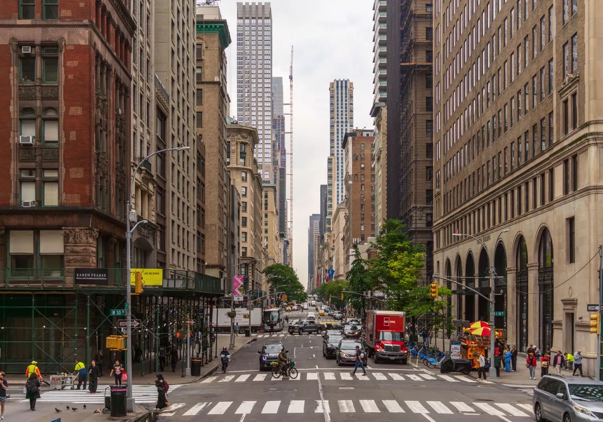 A busy street view of Midtown Manhattan with historic and modern buildings, pedestrians, and traffic.
